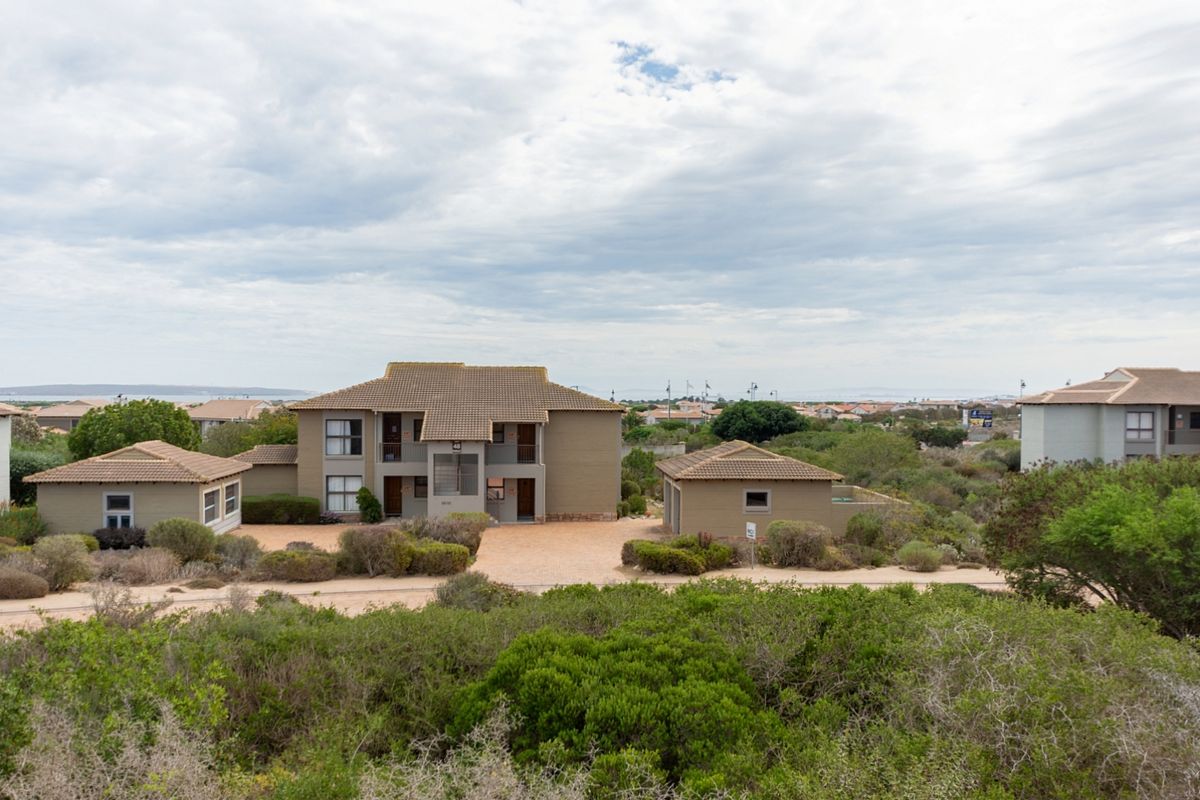An elevated aerial view of a residential apartment complex featuring tiled roofs, paved driveways, and established surrounding gardens.