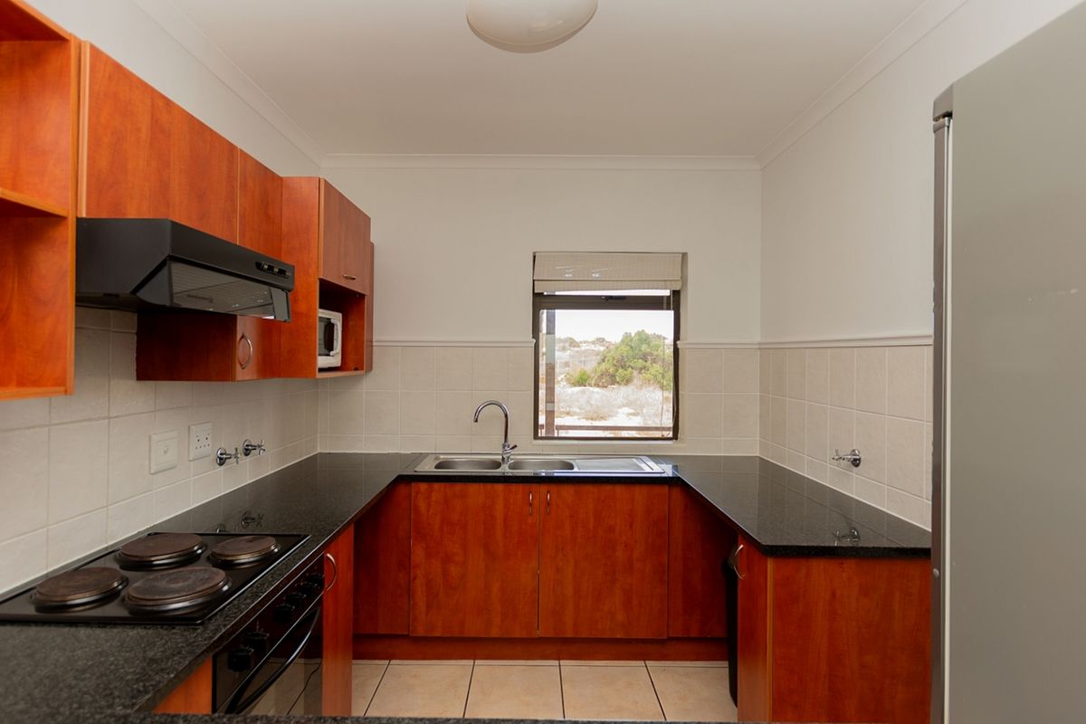 A functional kitchen featuring wood-finish cabinetry, granite countertops, a double sink, and built-in electric cooking appliances with tiled splashbacks.