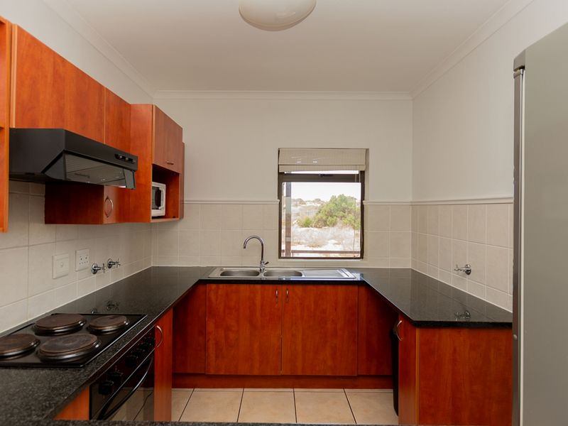 A functional kitchen featuring wood-finish cabinetry, granite countertops, a double sink, and built-in electric cooking appliances with tiled splashbacks.