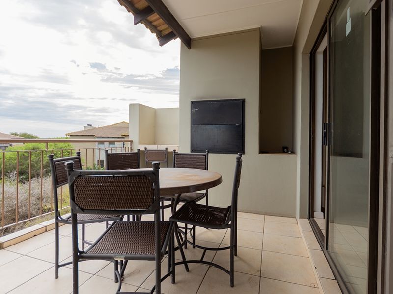 Covered balcony featuring a built-in braai, tiled flooring, and metal balustrade, offering an outdoor space accessible via sliding glass doors.