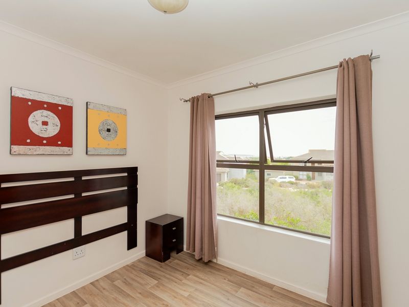 A bright bedroom featuring laminate flooring, neutral walls, and an aluminium window frame with curtain rod, offering a clean and functional living space.