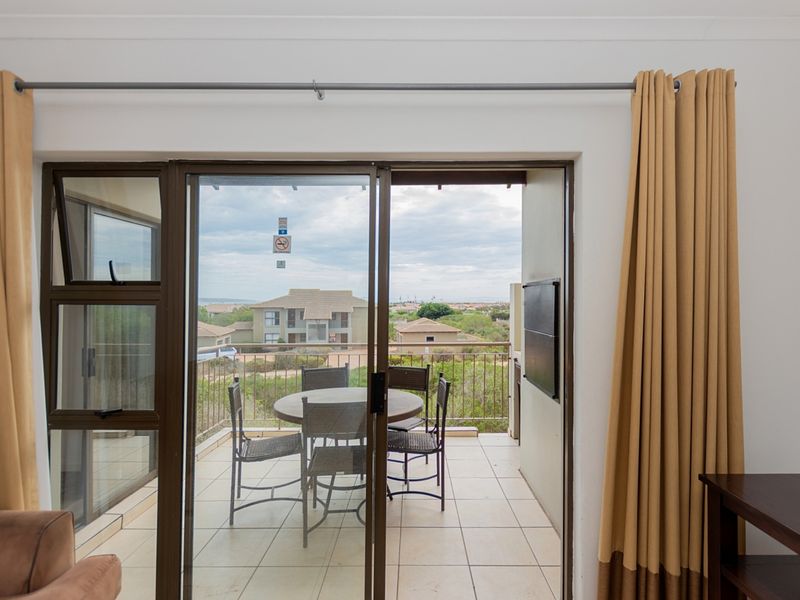 A covered balcony featuring tiled flooring and a metal balustrade, offering an outdoor seating area with views of the surrounding residential complex.