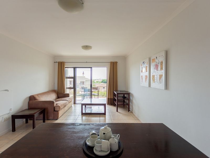 A bright living room featuring tiled flooring and a sliding glass door that opens to an outdoor balcony area.