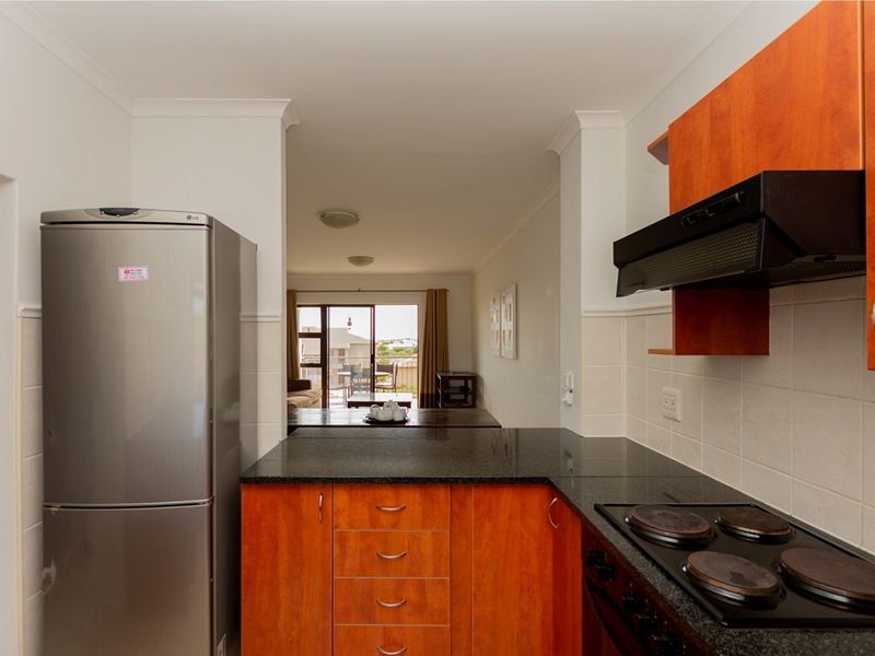 A functional kitchen featuring wood-finish cabinetry, granite countertops, and a built-in electric hob with an extractor fan, flowing into the adjacent living area.