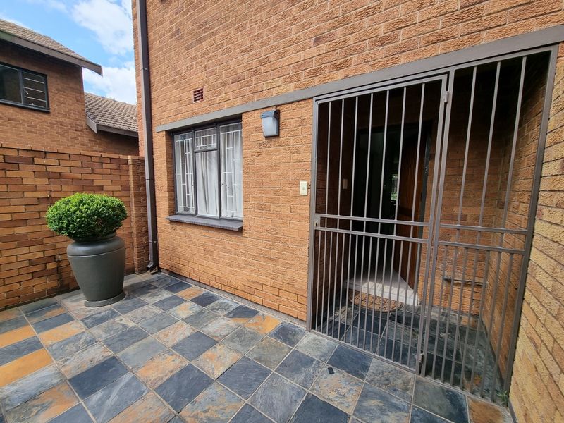 Front entrance area of the townhouse featuring a paved patio, brick facade, and a secure metal gate.