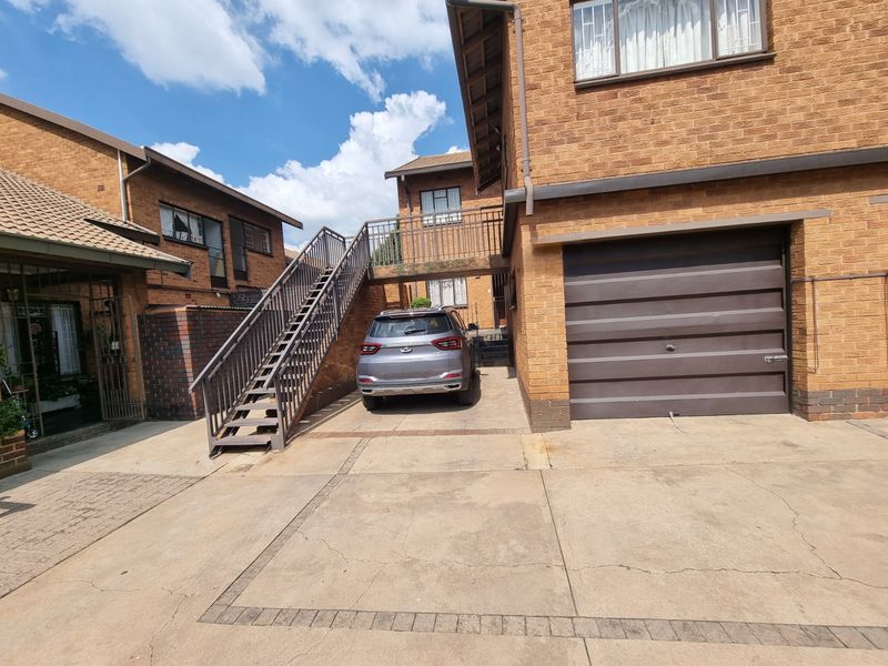Front exterior view of a brick townhouse featuring a garage, paved driveway, and an external staircase leading to the upper level.
