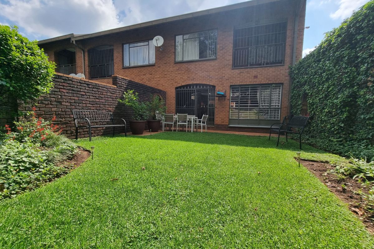 Rear view of the townhouse featuring a private garden with a lawn, brick boundary wall, and security bars on the windows.