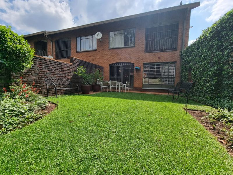 Rear view of the townhouse featuring a private garden with a lawn, brick boundary wall, and security bars on the windows.