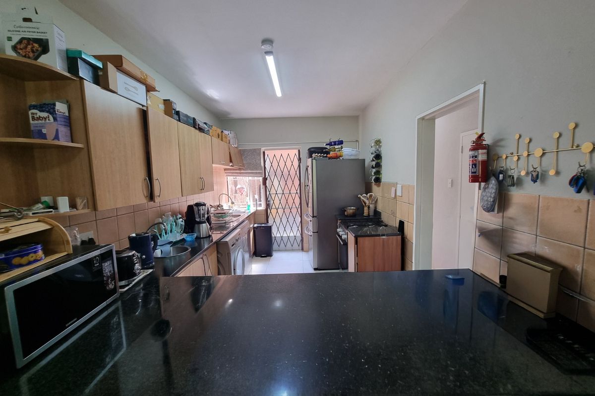 Functional kitchen featuring laminate cabinetry, granite countertops, tiled backsplash, and a security gate leading to the exterior.