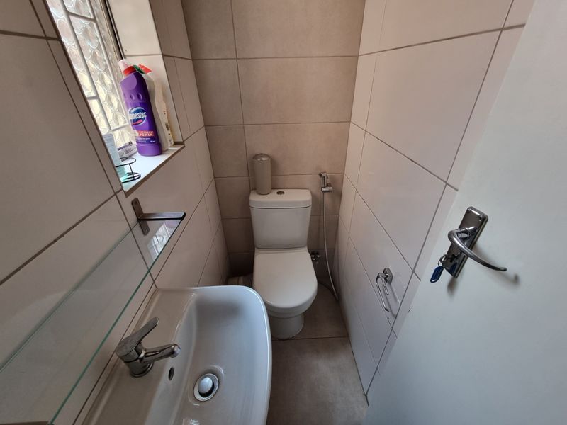 Compact guest bathroom featuring a modern toilet, wall-mounted basin with mixer tap, bidet spray, and neutral floor-to-ceiling wall tiles.