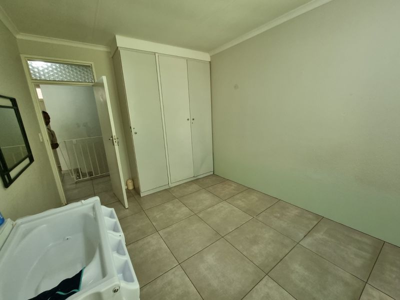 A clean, empty bedroom featuring neutral tiled flooring, built-in cupboards, and coved ceiling details, offering a blank canvas for personalization.