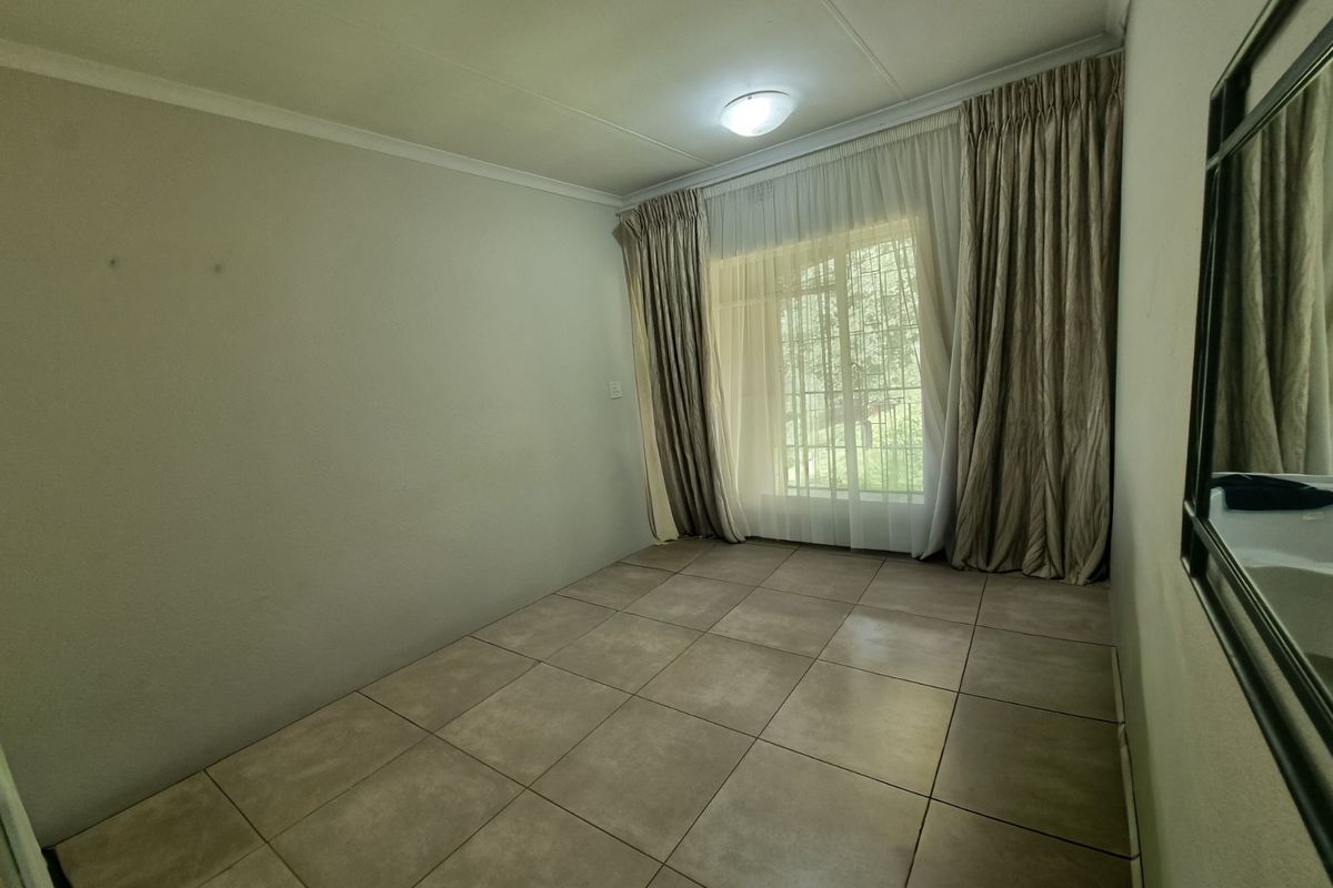 A vacant bedroom featuring neutral tiled flooring, large window with security bars, and installed curtain tracks, offering a clean and versatile living space.