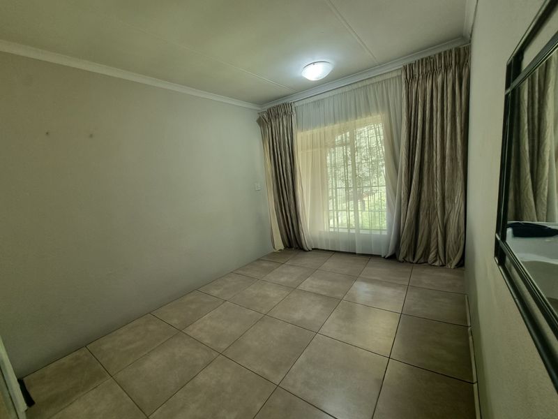 A vacant bedroom featuring neutral tiled flooring, large window with security bars, and installed curtain tracks, offering a clean and versatile living space.