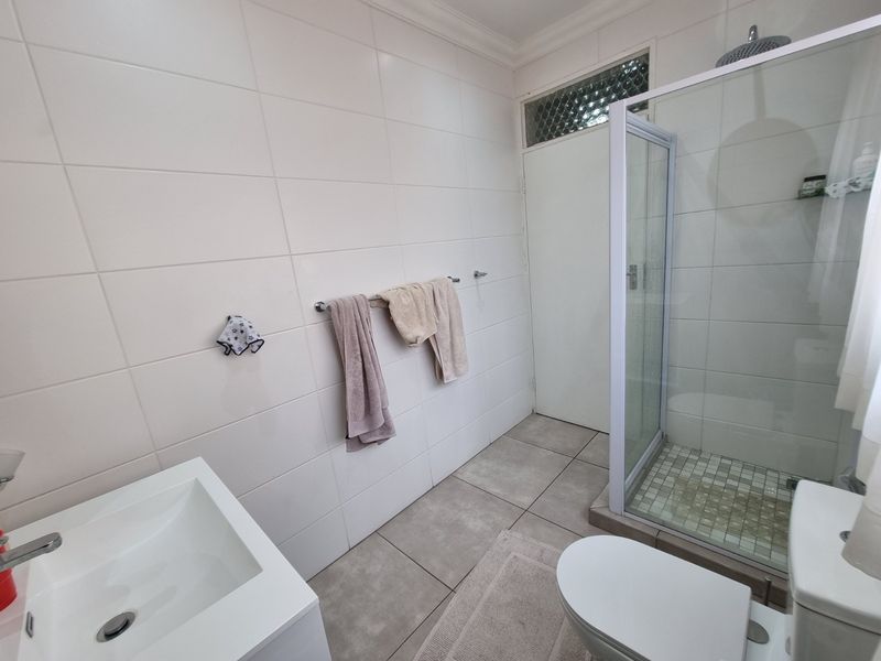 A functional bathroom featuring a glass-enclosed shower with a rain shower head, a modern vanity basin, and neutral wall and floor tiling.