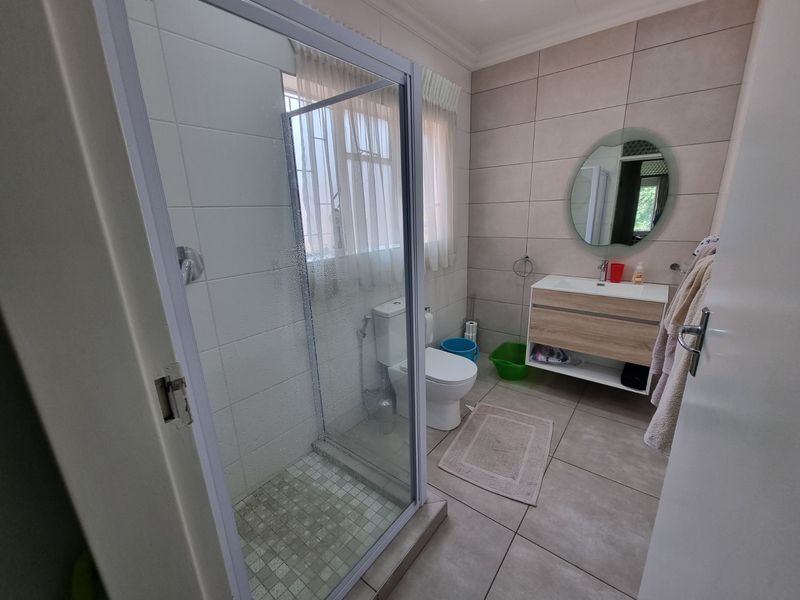 A modern bathroom featuring a glass-enclosed shower, a contemporary wall-mounted vanity with basin, and neutral floor-to-ceiling tiling.
