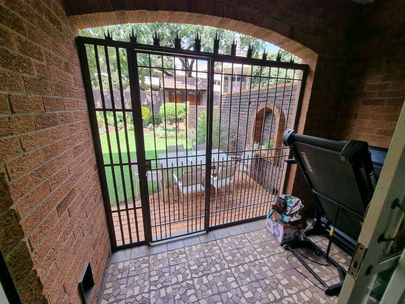 A covered patio area featuring brick archway detailing, tiled flooring, and a secure metal gate leading out to a private garden space.