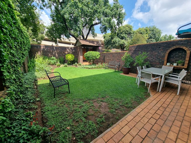 A private rear garden featuring a paved patio area, established lawn, and brick boundary walls with a decorative built-in arch.