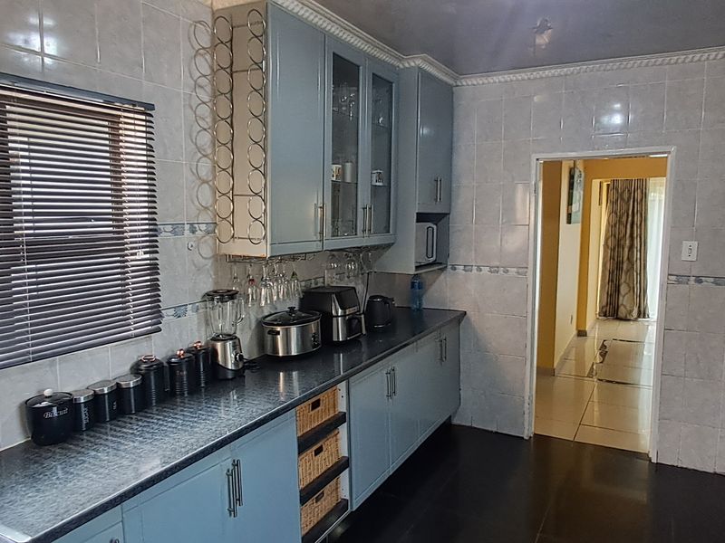 A functional kitchen featuring blue built-in cabinetry, tiled wall finishes, and dark countertops, providing a practical workspace with direct access to the hallway.