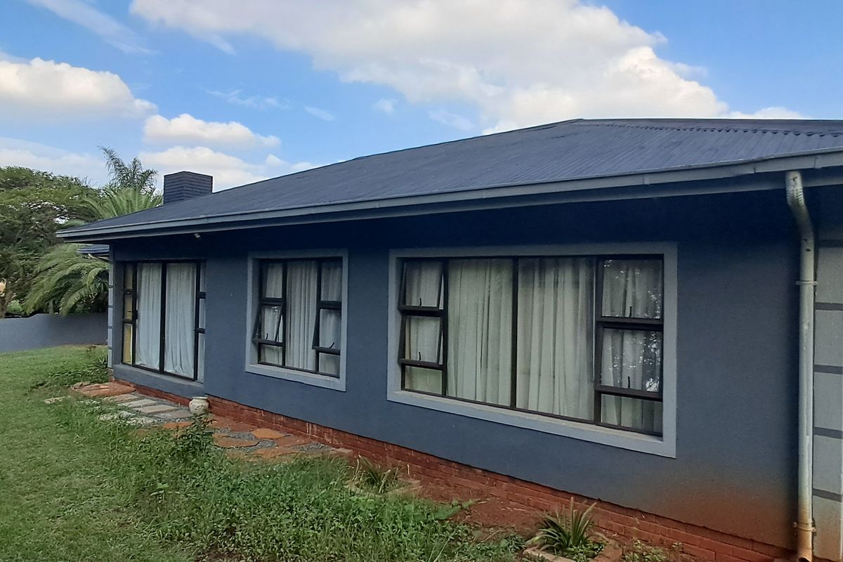 Rear view of a single-story house featuring a dark-painted exterior, corrugated metal roof, and aluminium-framed windows and sliding doors set in a garden.