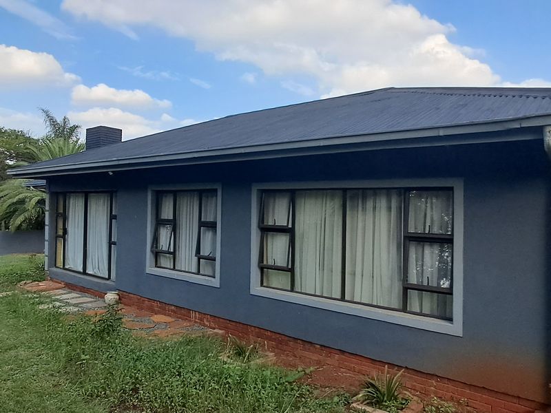 Rear view of a single-story house featuring a dark-painted exterior, corrugated metal roof, and aluminium-framed windows and sliding doors set in a garden.
