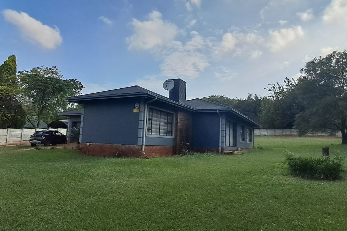 Rear view of the property featuring a dark-painted exterior, metal roofing, a chimney, and a spacious surrounding garden with boundary walling.
