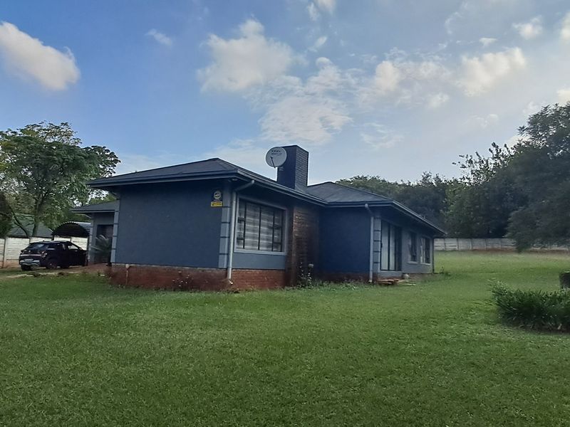 Rear view of the property featuring a dark-painted exterior, metal roofing, a chimney, and a spacious surrounding garden with boundary walling.
