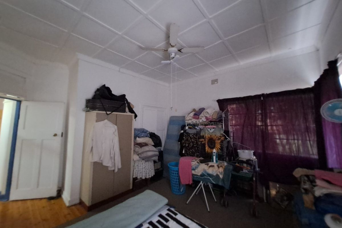 A bedroom featuring timber flooring, a ceiling fan, and a panelled ceiling, currently used for storage.