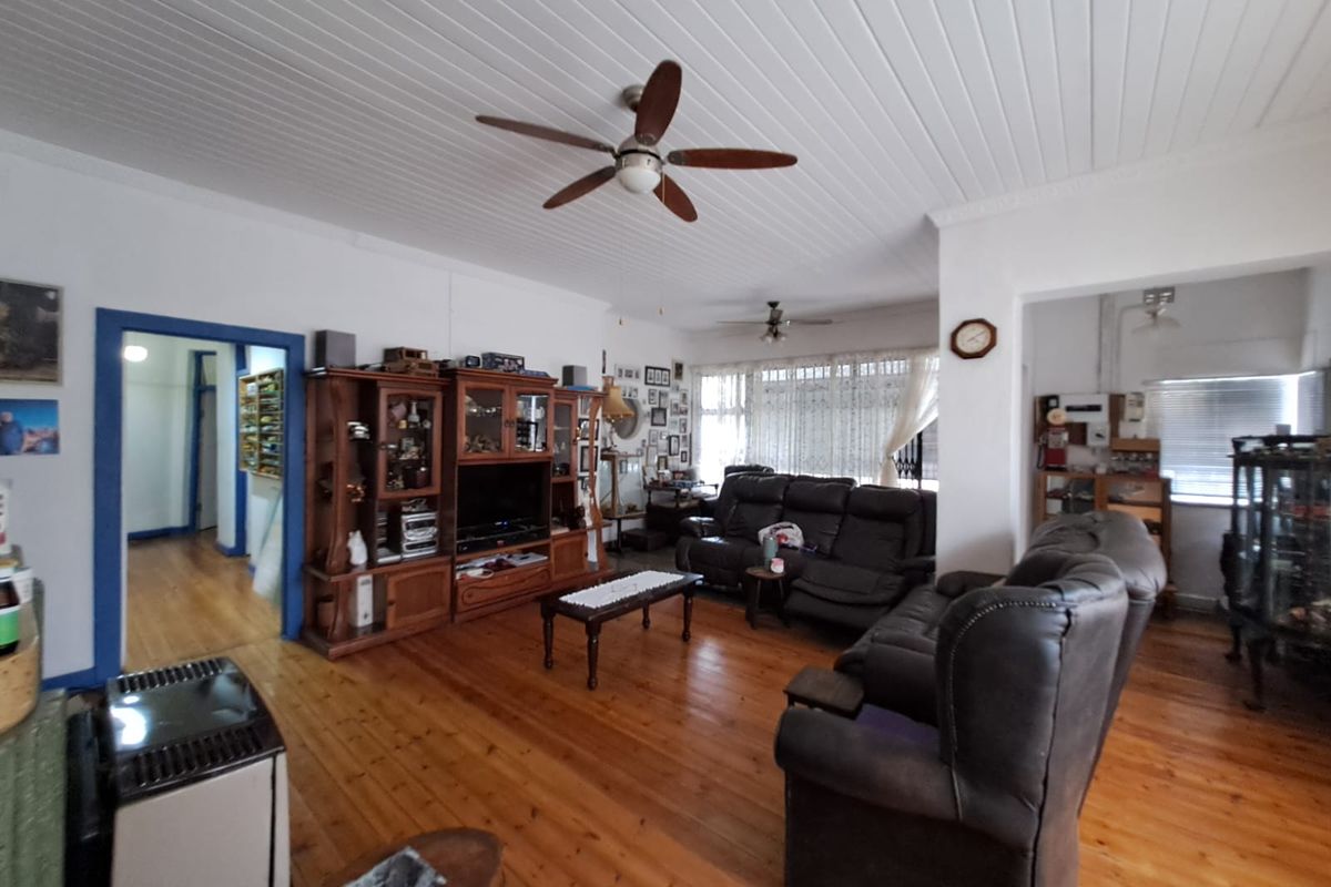 Spacious living room featuring polished timber flooring, a classic tongue and groove ceiling, and a ceiling fan, offering a warm and traditional atmosphere.