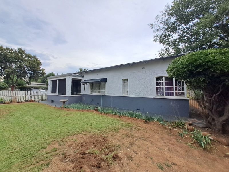 Rear view of a single-story house featuring a covered patio, textured exterior walls, and a garden area with established trees.
