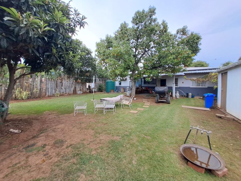 A spacious rear garden featuring a lawn, mature trees, a water tank, and perimeter fencing, offering a functional outdoor space.