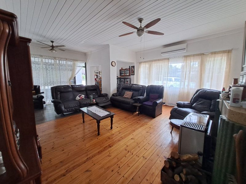 Spacious living room featuring polished timber flooring, tongue and groove ceiling, ceiling fans, and a built-in wood burning stove.