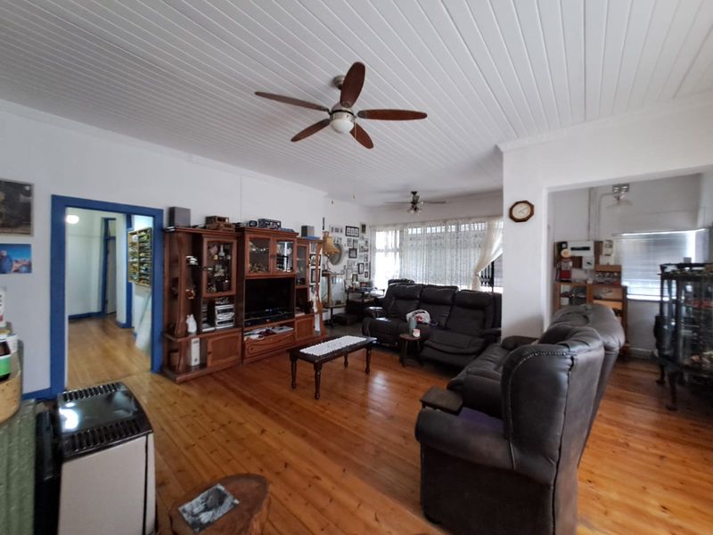 Spacious living room featuring polished timber flooring, a ceiling fan, and a classic tongue and groove ceiling design.