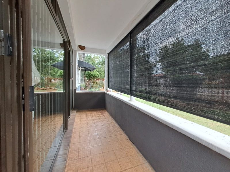 A covered patio area featuring tiled flooring, sliding glass doors, and a fixed shade cloth screen overlooking the garden.