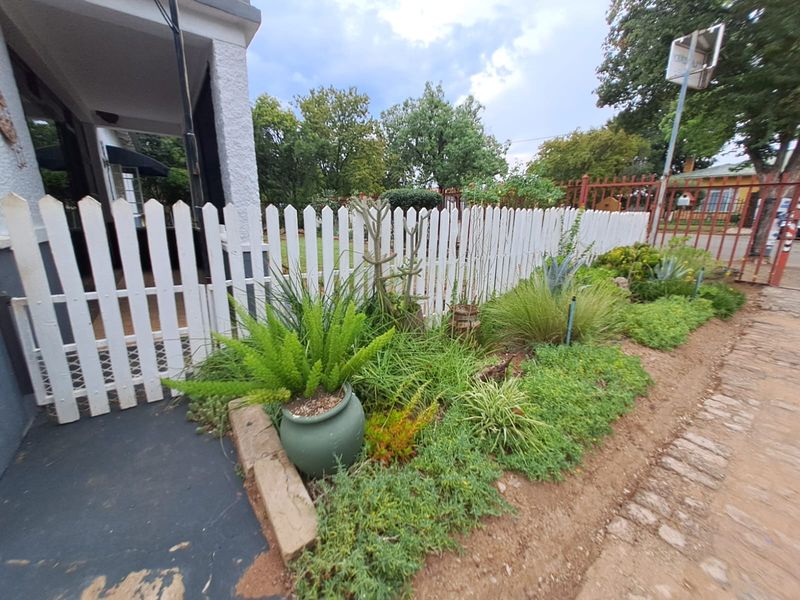 Front garden area featuring a white picket fence, paved driveway, and access to a covered porch entrance.