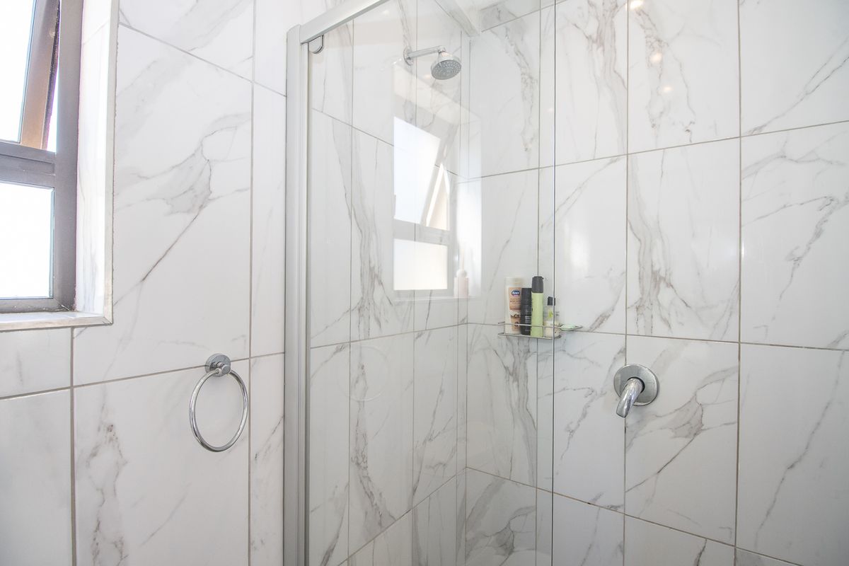 A modern bathroom featuring a glass-enclosed shower with marble-look wall tiles and contemporary chrome fixtures.