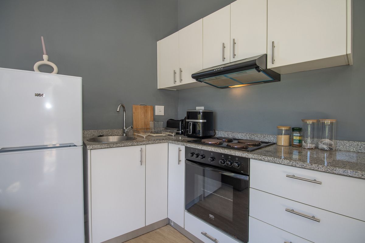 A compact, modern kitchen featuring white cabinetry, granite countertops, a built-in oven, electric hob, and an extractor fan.