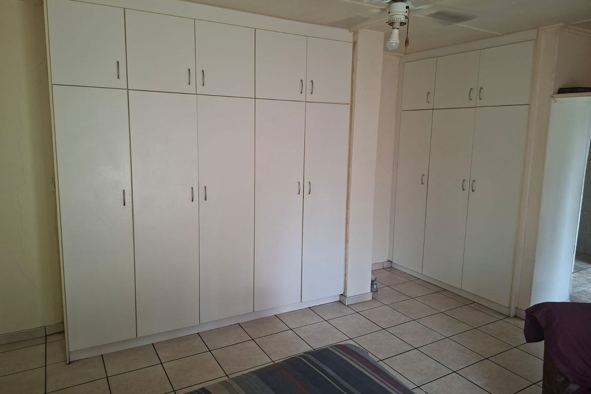 Bedroom featuring extensive white built-in cupboards, tiled flooring, and a ceiling fan. The room shows signs of wear and requires cosmetic updates.