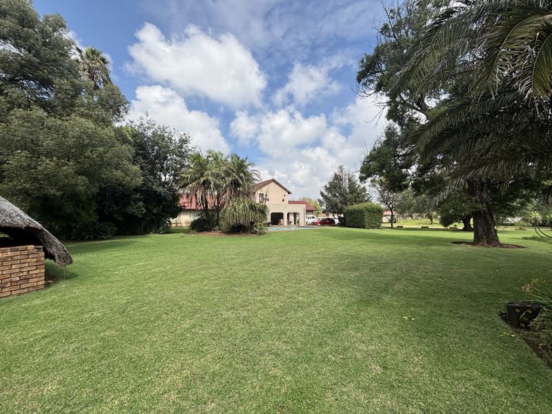 Expansive, well-maintained garden featuring mature trees, a large lawn, and a traditional thatched lapa structure, providing a serene outdoor setting.