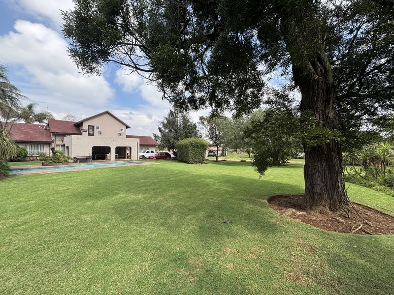 Spacious rear garden featuring a well-maintained lawn, mature trees, and a swimming pool adjacent to the covered patio area of the main residence.