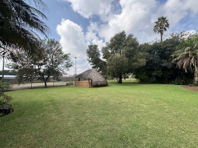 Expansive green garden featuring a traditional thatched lapa structure, mature trees, and perimeter fencing on a small holding property.