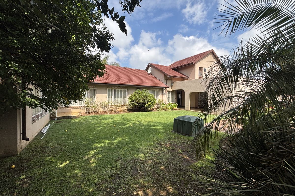 A view of the rear elevation of the property featuring a tiled roof, security bars on windows, and a spacious garden area.
