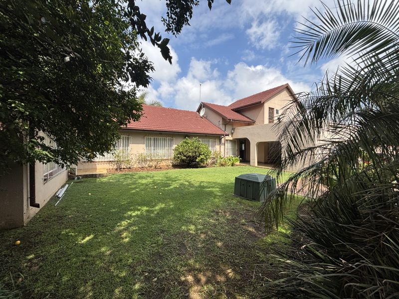 A view of the rear elevation of the property featuring a tiled roof, security bars on windows, and a spacious garden area.