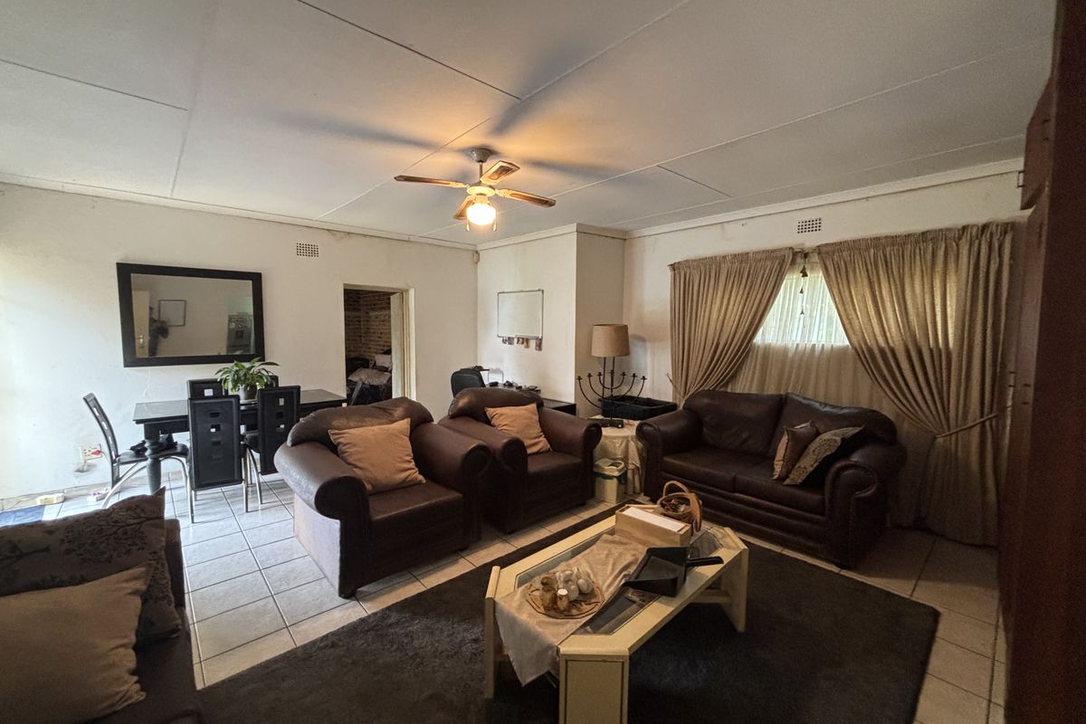 Spacious living area featuring tiled flooring and a ceiling fan, requiring some cosmetic updates to the ceiling and walls.