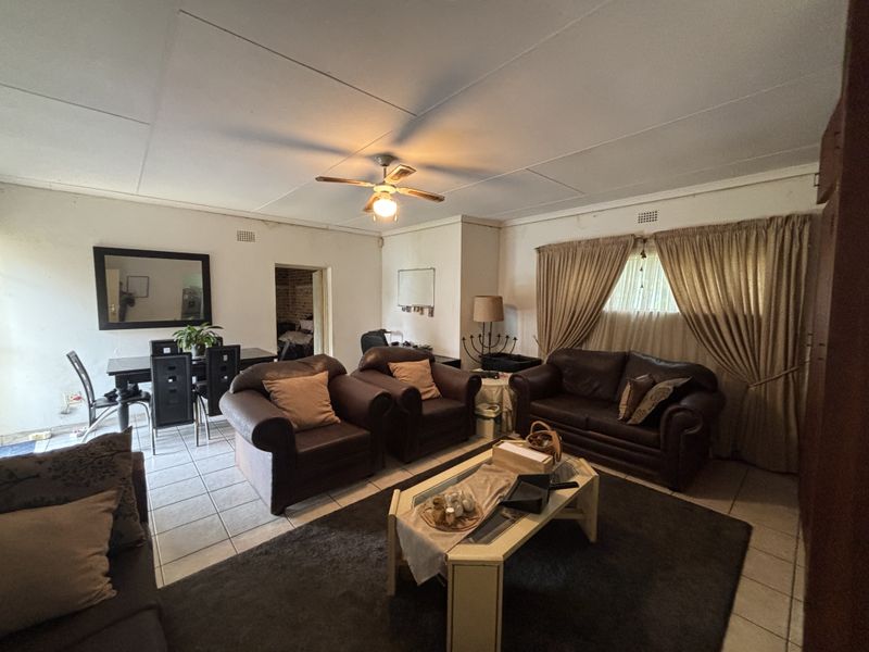 Spacious living area featuring tiled flooring and a ceiling fan, requiring some cosmetic updates to the ceiling and walls.