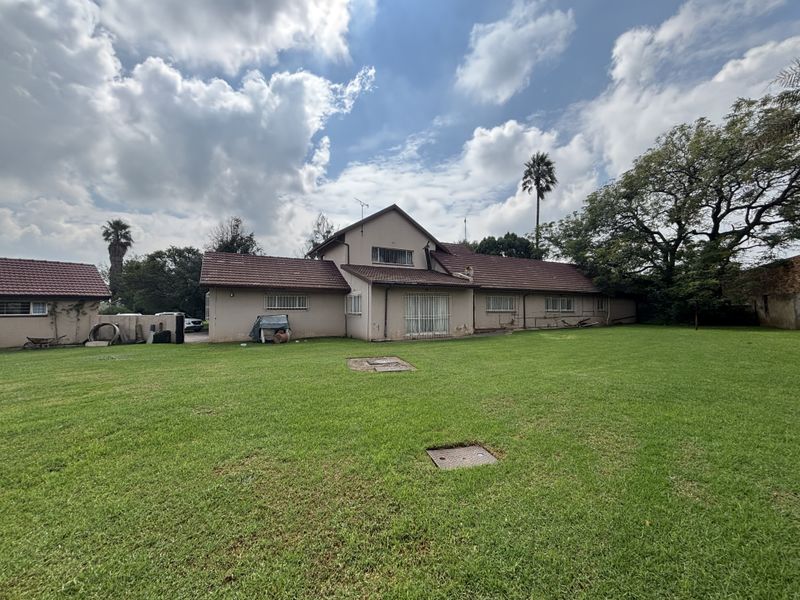 Rear view of the property showing the main dwelling, tiled roof, security bars on windows, and a large surrounding lawn area.