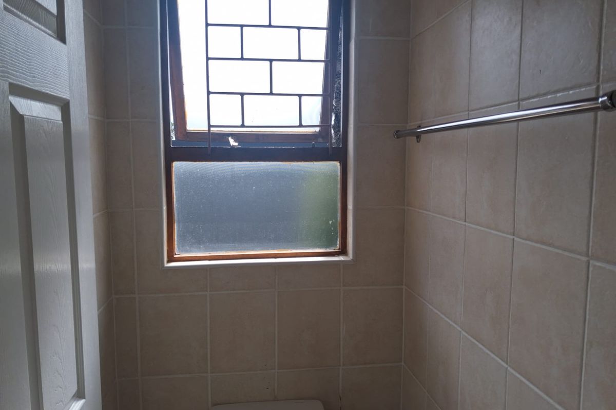 A compact bathroom featuring neutral wall tiles, a window with security bars, and a towel rail.