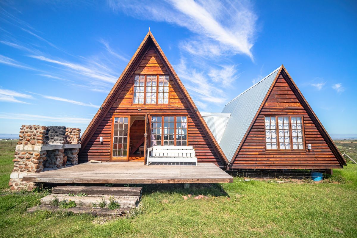 A charming A-frame timber cabin featuring a wooden deck, stone outdoor fireplace, and expansive rural views.