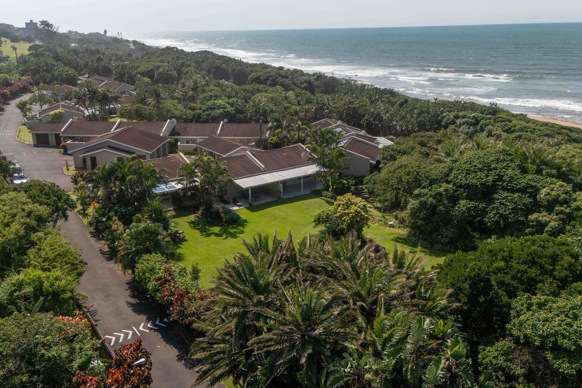 Aerial view of a coastal townhouse complex featuring tiled roofs, paved driveways, and lush garden spaces situated near the ocean.