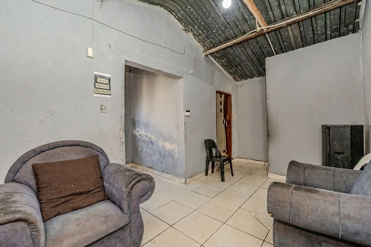A living area featuring tiled flooring and an exposed corrugated metal ceiling, currently showing significant signs of wear and wall surface deterioration.