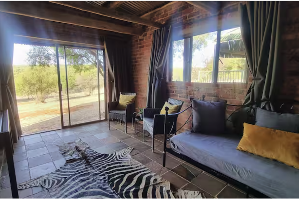 Rustic living area featuring exposed brick walls, timber ceiling beams, tiled flooring, and large sliding glass doors opening to the surrounding farm landscape.